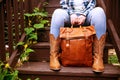 woman is holding a brown leather backpack while sitting on the steps. Close-up of hands and leather cowboy boots