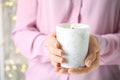 Woman holding burning candle with wooden wick against festive lights, closeup Royalty Free Stock Photo