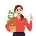 Woman holding cannabis plant in pot and giving peace sign as she is supporting the use of cannabis. Weed or marijuana Royalty Free Stock Photo