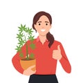 Woman holding cannabis plant in pot and giving thumb up as she is supporting the use of cannabis. Weed or marijuana