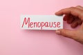 Woman holding card with word Menopause on pink background, closeup