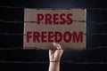 Woman holding cardboard paper with PRESS FREEDOM text and rusty sharp bare wire on dark background, conceptual image