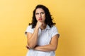 Woman holding chin and musing, looking away with thoughtful facial expression.