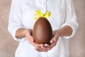 Woman holding chocolate Easter egg with bow knot on color background