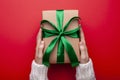 Woman holding Christmas gift box wrapped in craft paper on color background. Female hands holding present for Christmas Royalty Free Stock Photo