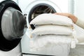 Woman holding clean white pillows in front of the drum of washing machine Royalty Free Stock Photo