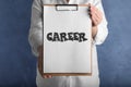 Woman holding clipboard with word CAREER on background, closeup