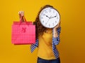 Woman holding clock in front of face and showing shopping bags Royalty Free Stock Photo