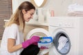 Woman holding container with laundry detergent capsules near washing machine indoors Royalty Free Stock Photo