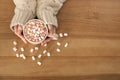 Woman holding cup of aromatic cacao with marshmallows on wooden background, top view