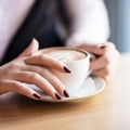 Woman holding cup of capuccino on wooden table.