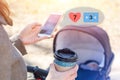 Woman holding cup of coffee to go and using smartphone during walk with baby carriage. Browsing social media, likes and messages. Royalty Free Stock Photo