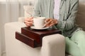 Woman holding cup of drink on sofa armrest wooden table at home, closeup Royalty Free Stock Photo