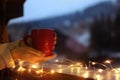 Woman holding cup of hot beverage on balcony decorated with Christmas lights, closeup with space for text