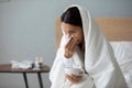 Woman holding cup with hot beverage and blows runny nose