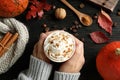 Woman holding cup with tasty pumpkin spice latte at wooden table, closeup