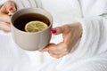 Woman holding cup of tea with lemon. Girl in white bathrobe holding brown mug of tea. Home comfort concept. Morning drink concept. Royalty Free Stock Photo