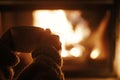 Woman holding cup of tea and warming up hands at cozy fireplace in dark evening room, close up. Fireplace heating in house,