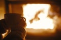 Woman holding cup of tea and warming up hands at cozy fireplace in dark evening room, close up. Fireplace heating in house,