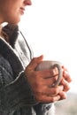 Woman holding cup of tea wearing gray woolly cardigan looking out of a window