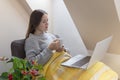 Woman holding cup and watching something on laptop sitting on a coach Royalty Free Stock Photo