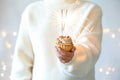 Woman holding cupcake with burning sparklers against blurred festive lights, closeup Royalty Free Stock Photo