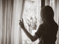 Woman holding the curtains open to look out of a large light window at home. Royalty Free Stock Photo