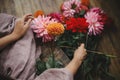 Woman holding dahlias flowers and sitting on wooden rustic bench, view above. Atmospheric moody image. Florist in linen dress