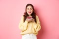 Woman holding delicious cake, licks her lips with closed eyes and dreamy face, wants to eat tasty dessert, standing