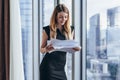 Woman holding documents, looking through papers, studying the report standing near window with view on skyscrapers Royalty Free Stock Photo