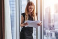 Woman holding documents, looking through papers, studying the report standing near window with view on skyscrapers Royalty Free Stock Photo