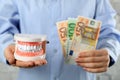 Woman holding educational dental typodont model and euro banknotes on light background, closeup. Expensive treatment