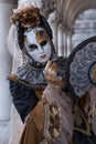 Woman holding fan and wearing mask and ornate gold and black costume under the arches at the Doges Palace during Venice Carnival