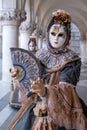 Woman mask holding fan and wearing ornate gold and black costume under the arches at the Doges Palace during Venice Carnival