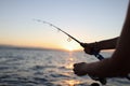 Woman holding fishing rod in her hands, sunset above sea in background. Royalty Free Stock Photo