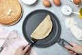 Woman holding frying pan with thin pancake at grey marble table, top view