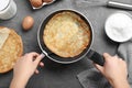 Woman holding frying pan with thin pancake at table, top view