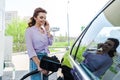 Woman holding fuel pump while refueling car with benzine and talking on smartphone