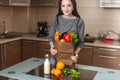 Woman holding full paper bag with products in hands on the background of the kitchen. Healthy and fresh organic food Royalty Free Stock Photo