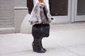 A woman holding a furry black purse and wearing black booties