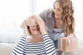 Woman holding gift and covering her mom`s eyes Royalty Free Stock Photo