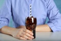 Woman holding glass of cola with ice and straw at white table against light blue background, closeup. Refreshing soda water Royalty Free Stock Photo