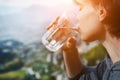 Woman holding glass of crystal clear natural water, drinking, nature mountain background