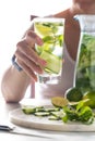 Woman holding a glass of cucumber water with bright sunlight in behind.