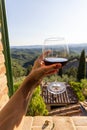 Woman holding a glass of red wine with beautiful landscape of Italy in a background on a sunny day. Royalty Free Stock Photo