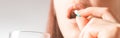 Woman holding glass of water and taking a capsule pill, close-up.