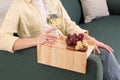 Woman holding glass of wine and snacks on sofa armrest wooden table at home, closeup Royalty Free Stock Photo