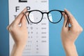 Woman holding glasses against eye chart on blue background, closeup. Ophthalmologist prescription Royalty Free Stock Photo