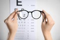 Woman holding glasses against eye chart on light background, closeup. Ophthalmologist prescription Royalty Free Stock Photo