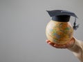 Woman holding a globe wearing a graduation cap.